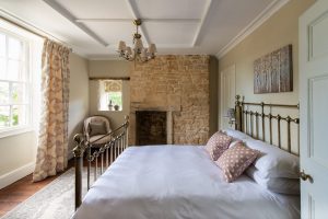 Bedroom with brass bedstead and exposed Cotswold stone fireplace